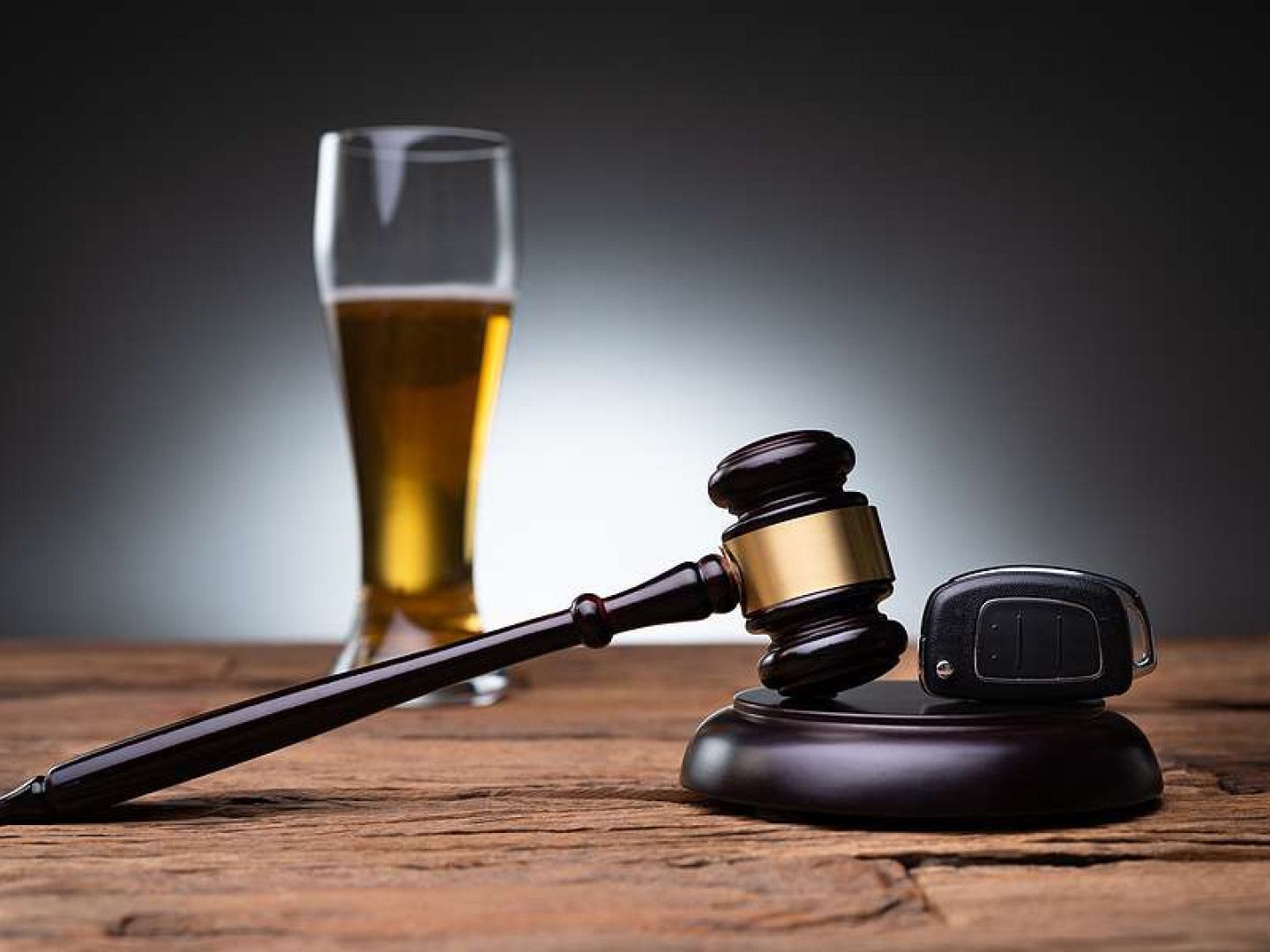 A wooden gavel and car keys rest on a textured table in front of a glass of beer, symbolizing legal consequences of DUI.