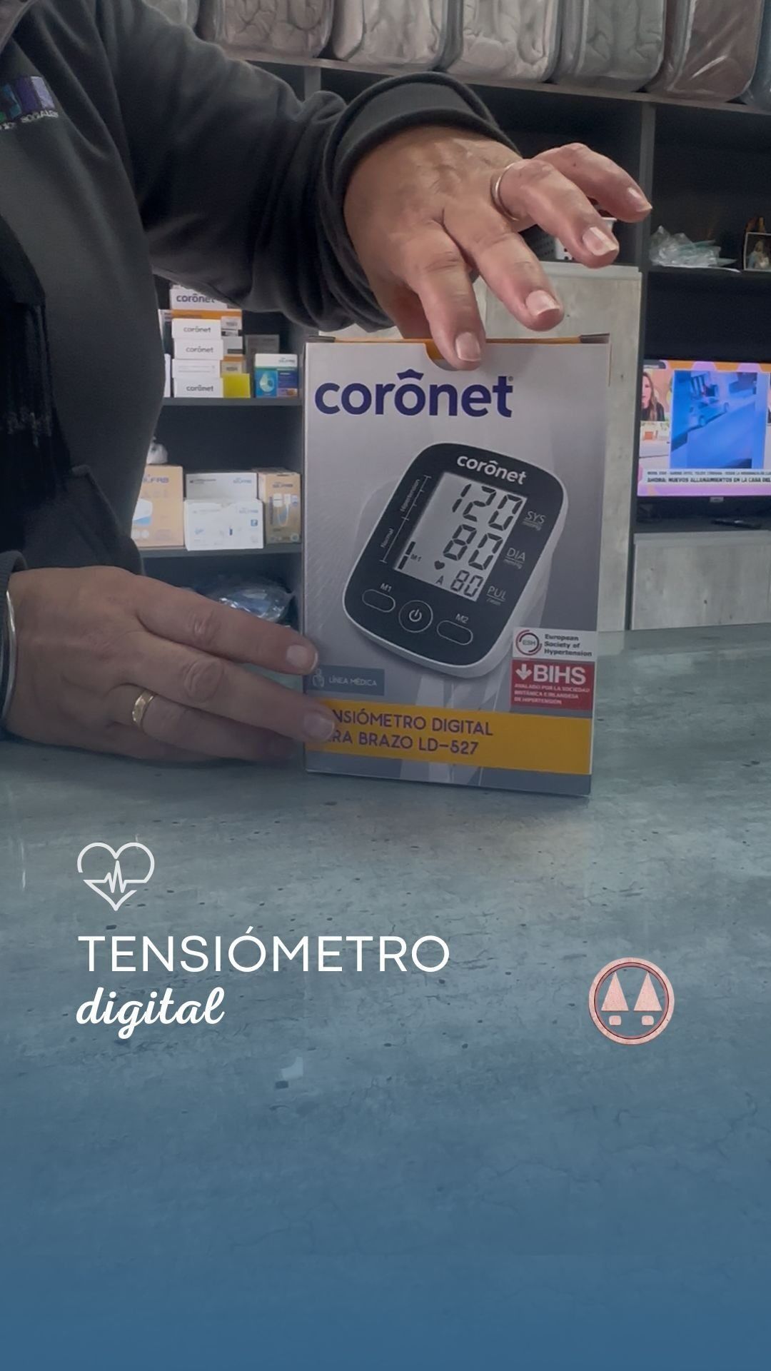 Manos sosteniendo una caja de un tensiómetro digital Coronet sobre una encimera, con el texto 