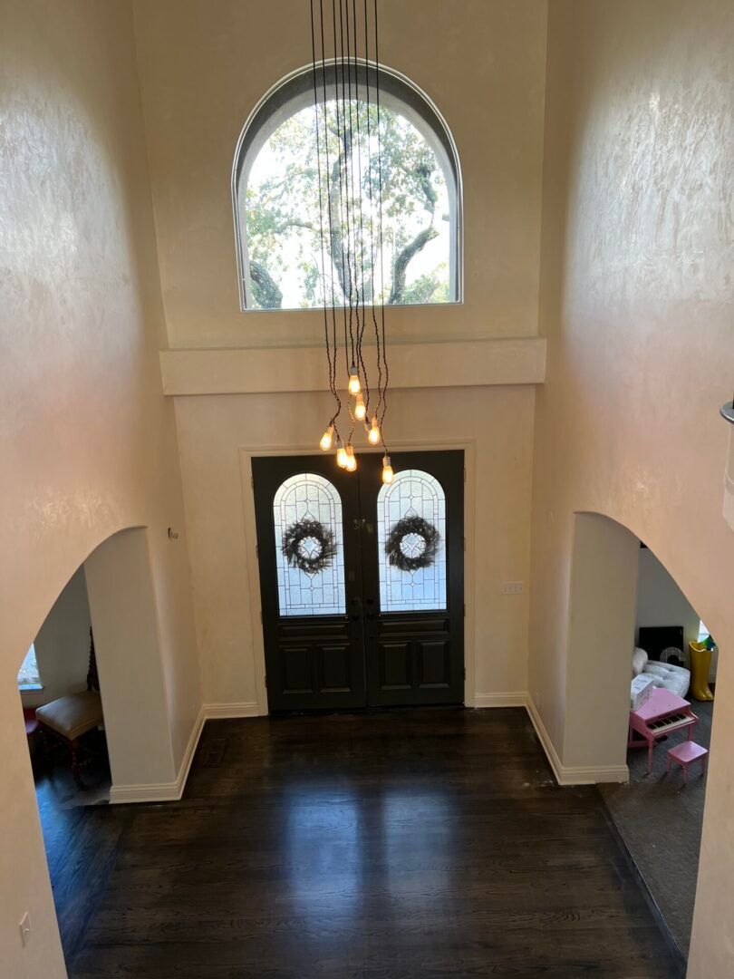 A large empty room with a chandelier hanging from the ceiling and a door with a wreath on it.