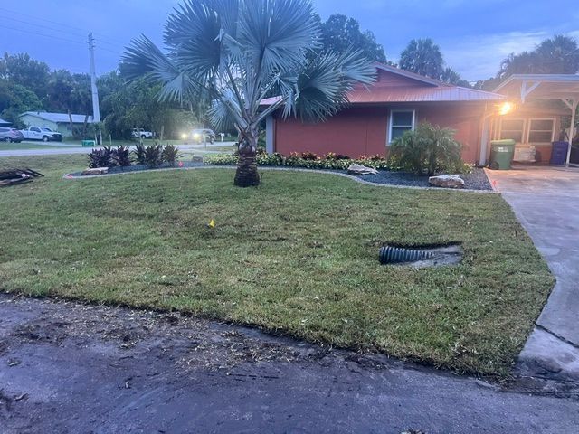 Front yard with a palm tree, trimmed lawn, driveway, and a house at dusk
