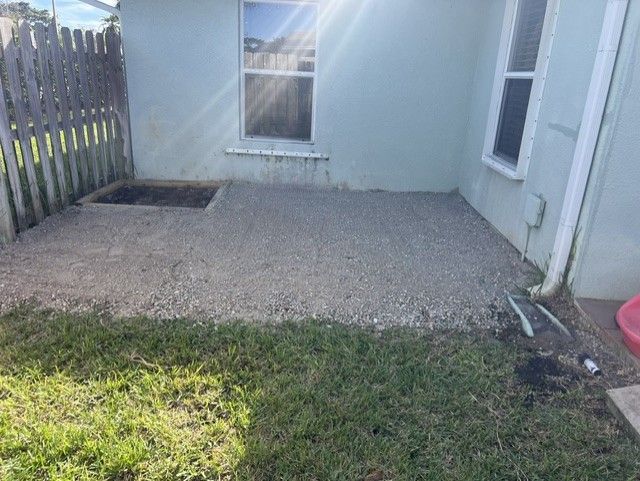 Small gravel patio beside a light blue house, with a grassy yard and wooden fence.