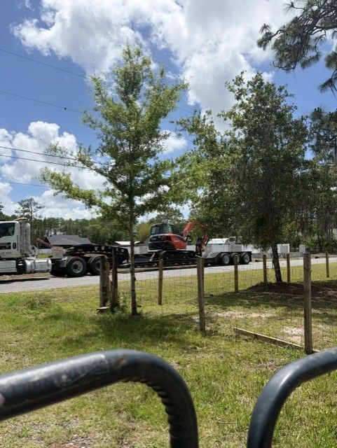 Tree-lined roadside with utility trucks parked under a partly cloudy sky