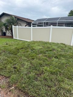 Backyard with grassy lawn, beige privacy fence, and house under cloudy sky