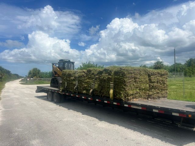 Flatbed trailer loaded with hay bales on a rural road under a cloudy sky