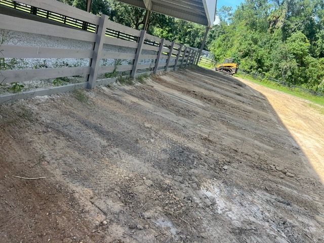 Empty dirt lot beside a metal-sided barn with trees in the background