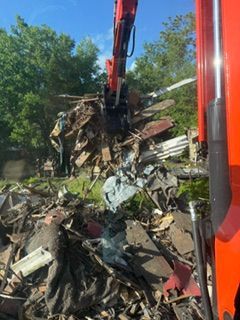 Crane lifting a pile of twisted metal debris outdoors under a blue sky