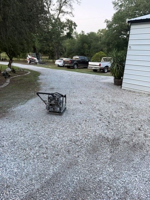 Gravel driveway with parked cars and a tipped-over black chair beside a white building.