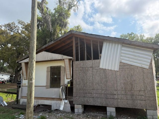 Partially damaged mobile home with a sagging roof and boarded exterior in a wooded lot