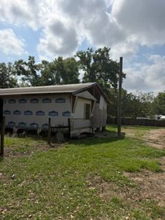 Small white house with a carport in a grassy rural yard under a cloudy sky