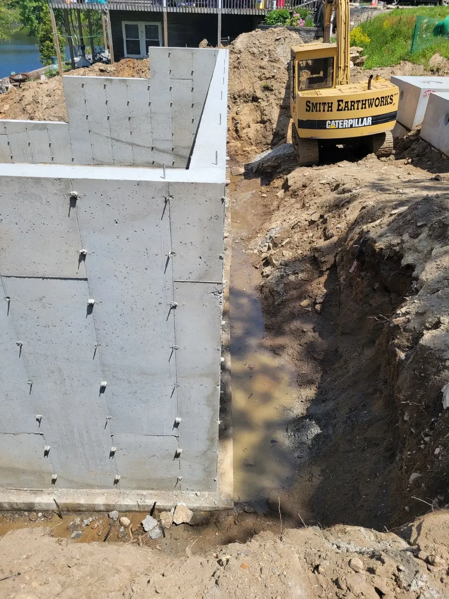 Construction site with concrete wall and excavator digging a trench beside it