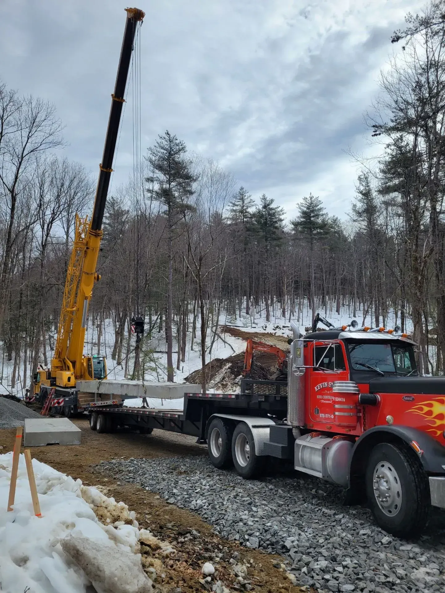 Crane truck lifting debris on a snowy roadside in a wooded area