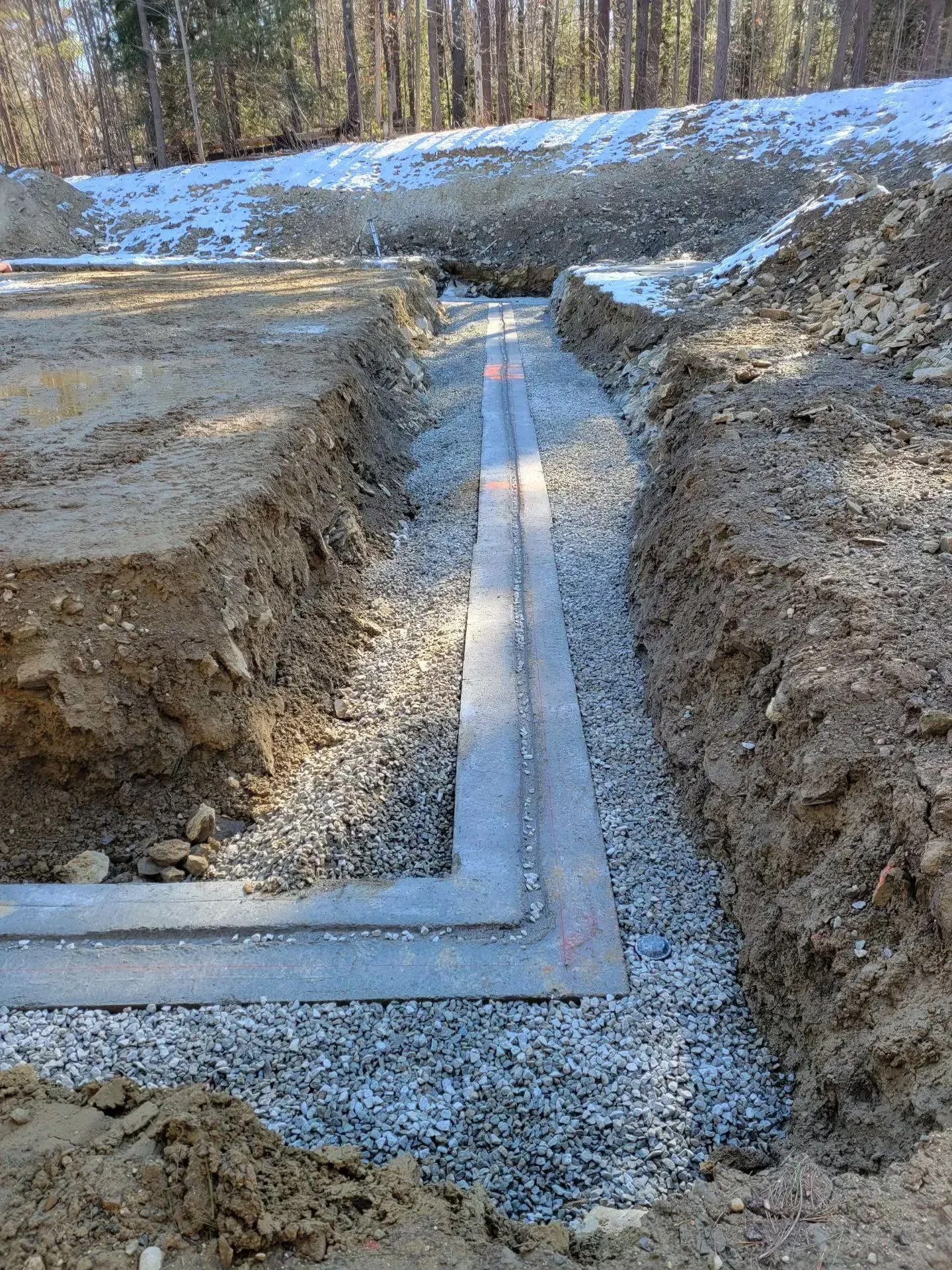 Trench with gravel and concrete footing in a snowy construction site, viewed from above