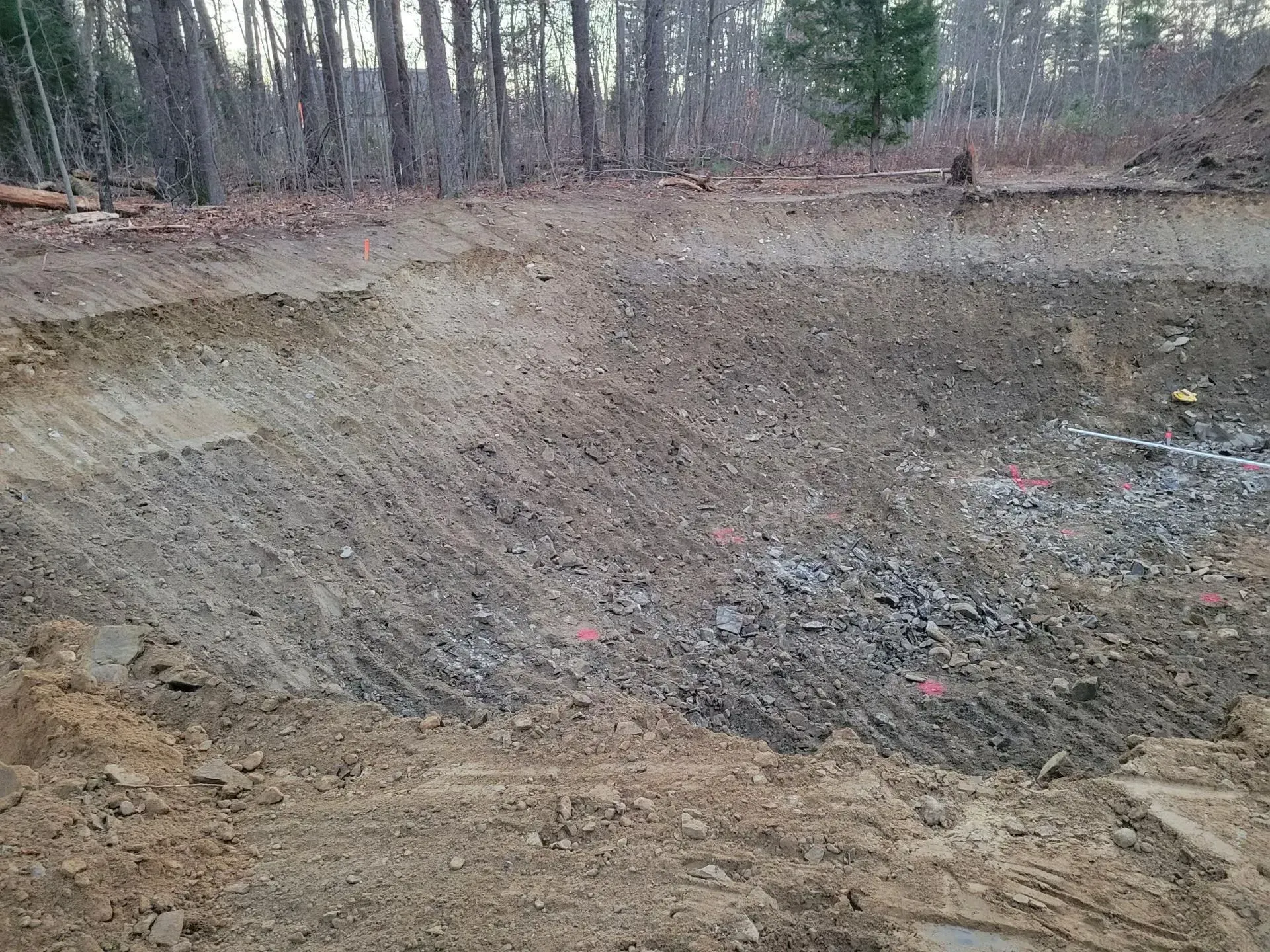 Large dirt pit with steep earthen walls in a wooded area, with trees in the background.