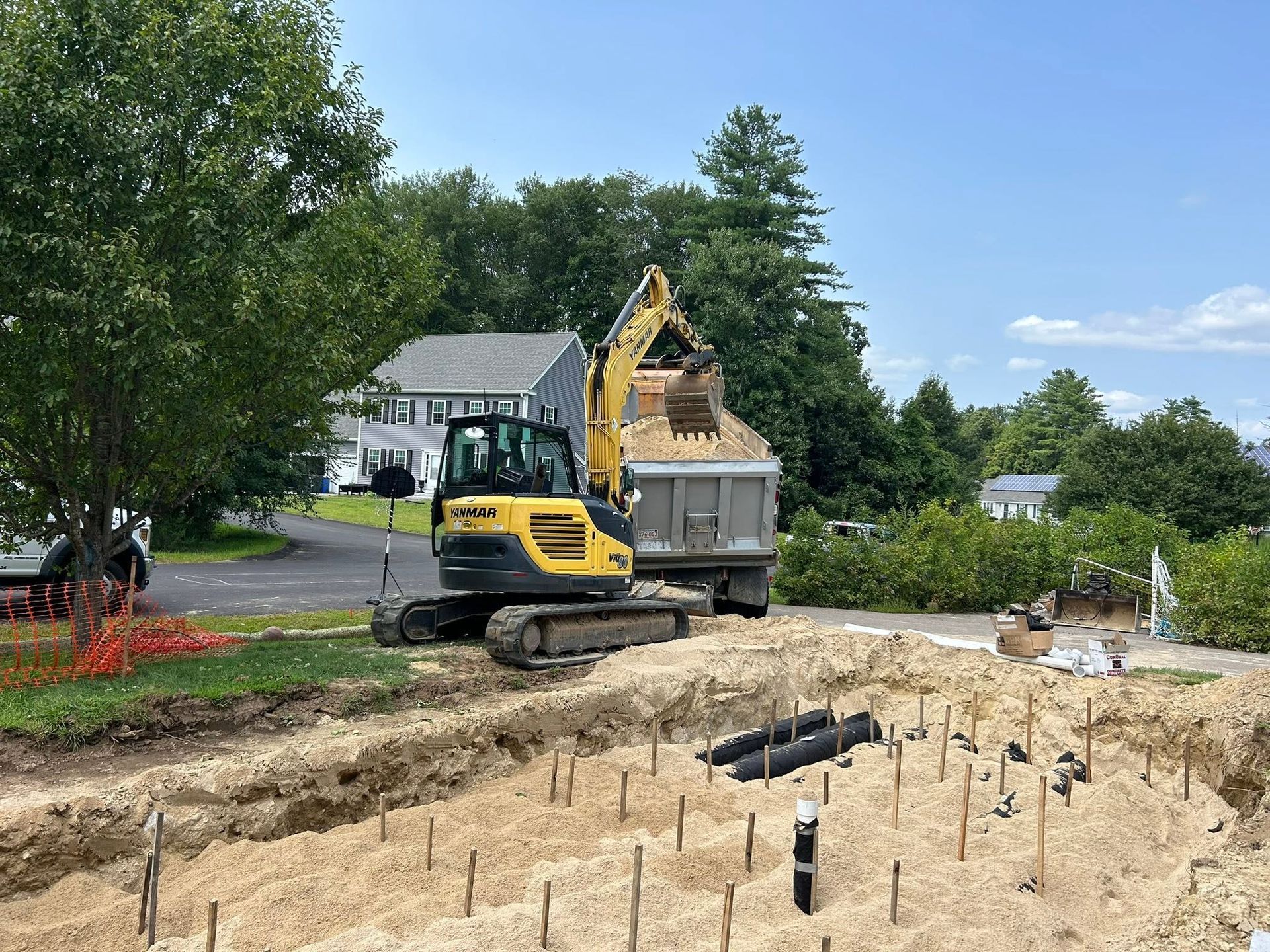 Excavator and dump truck at a residential construction site with foundation holes and stacked materials
