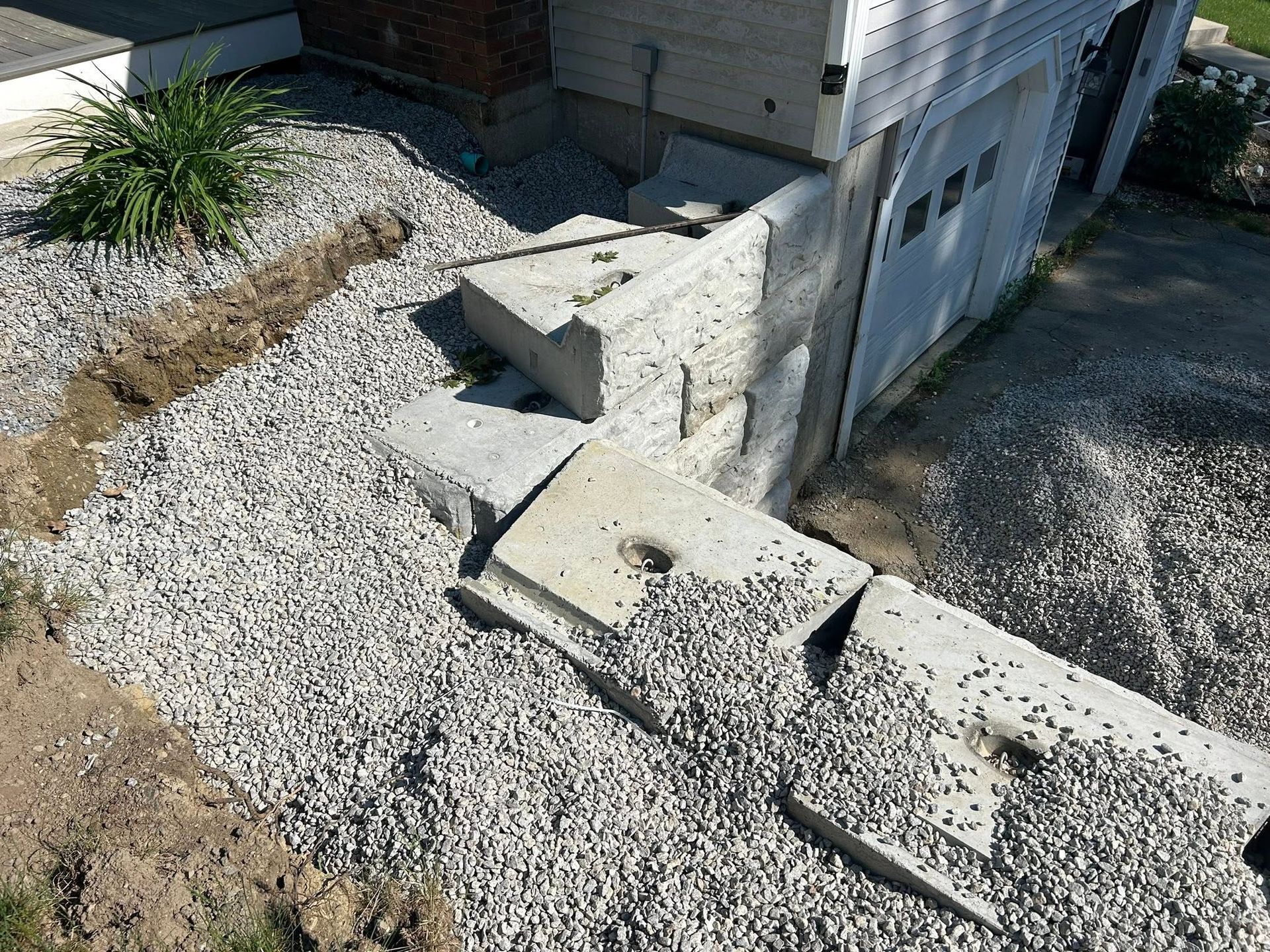 Concrete retaining wall beside a house, with a gravel yard and steps leading up to a doorway
