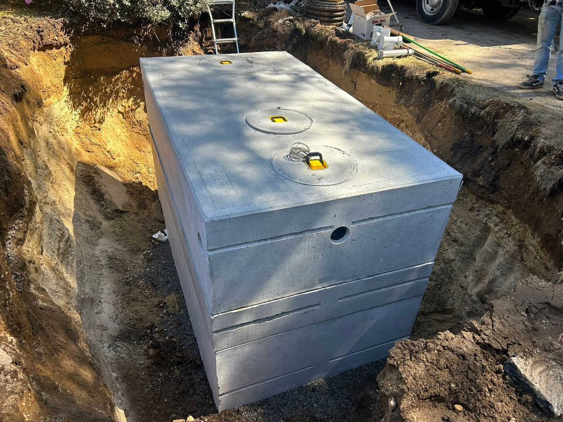 Rectangular gray septic tank installed in a dirt excavation on a construction site.