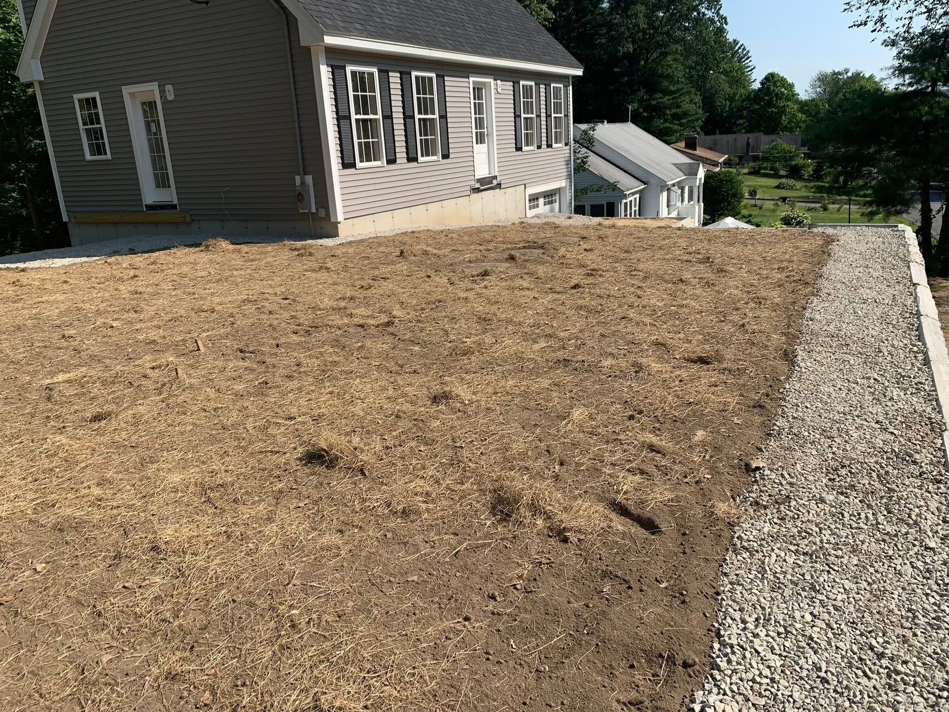 Freshly spread brown mulch beside a house, with a gravel border and lawn in the background