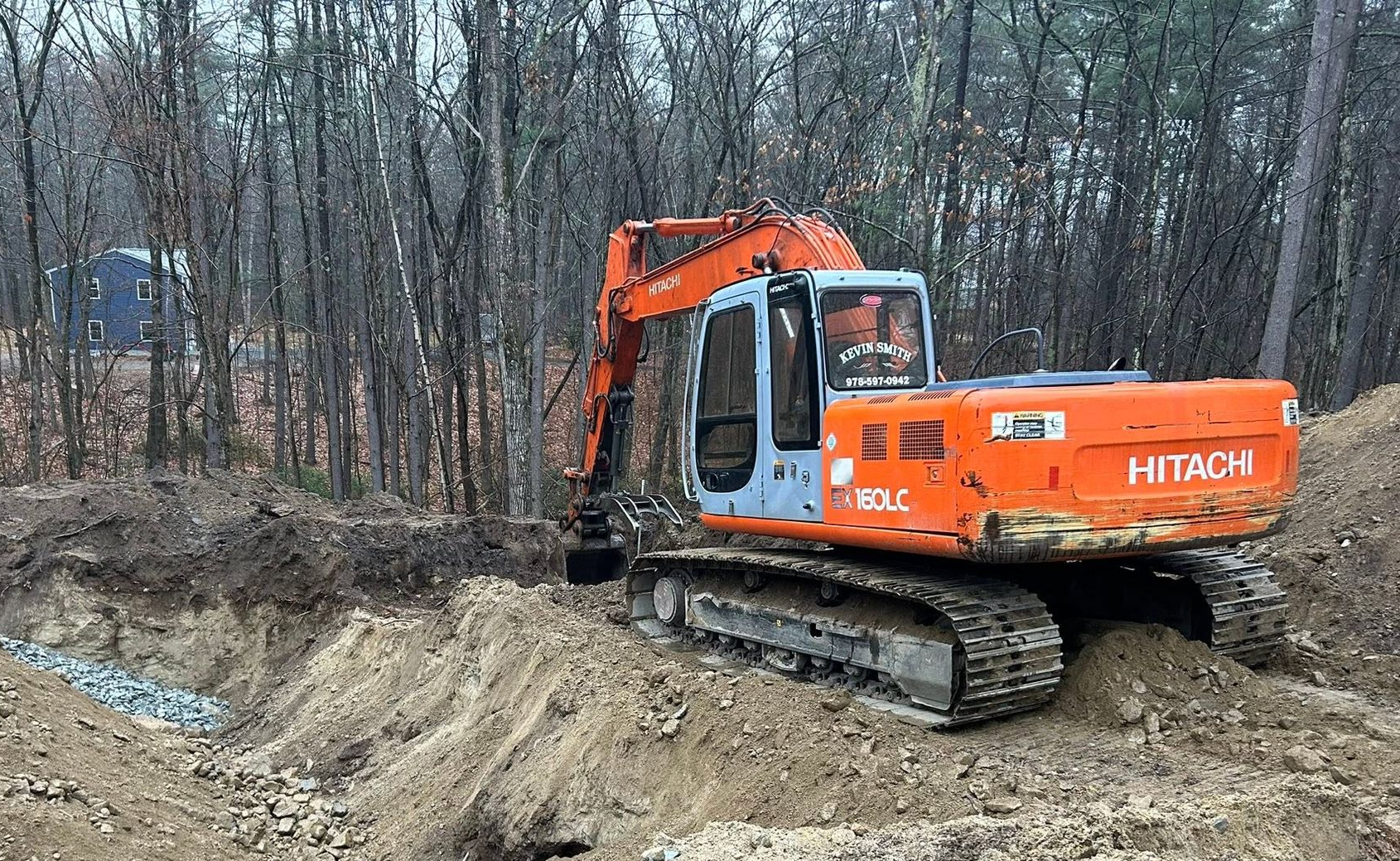 Orange excavator working in a muddy forest clearing beside a ditch