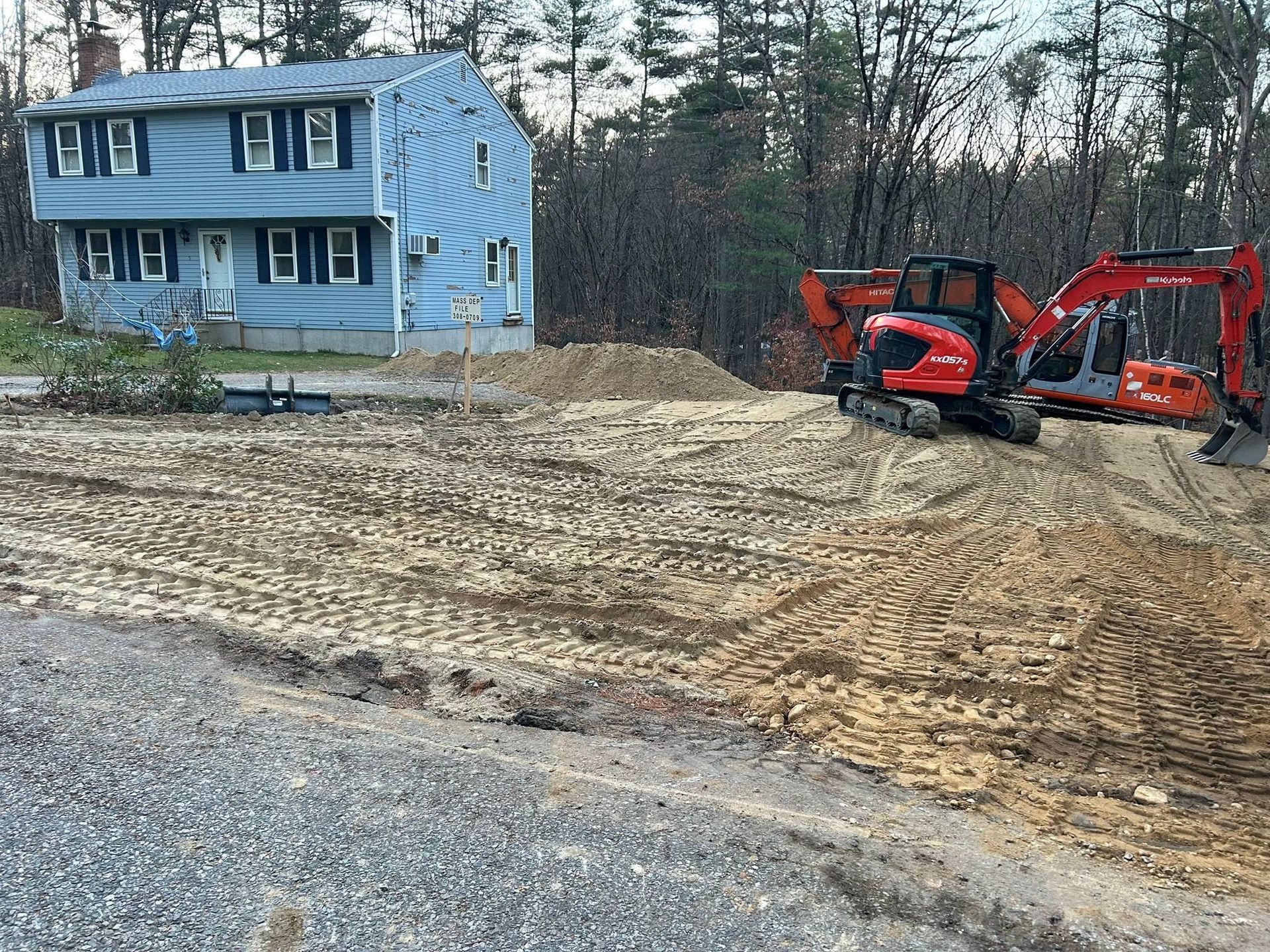 Blue house beside a cleared dirt lot with red excavators and a gravel foreground