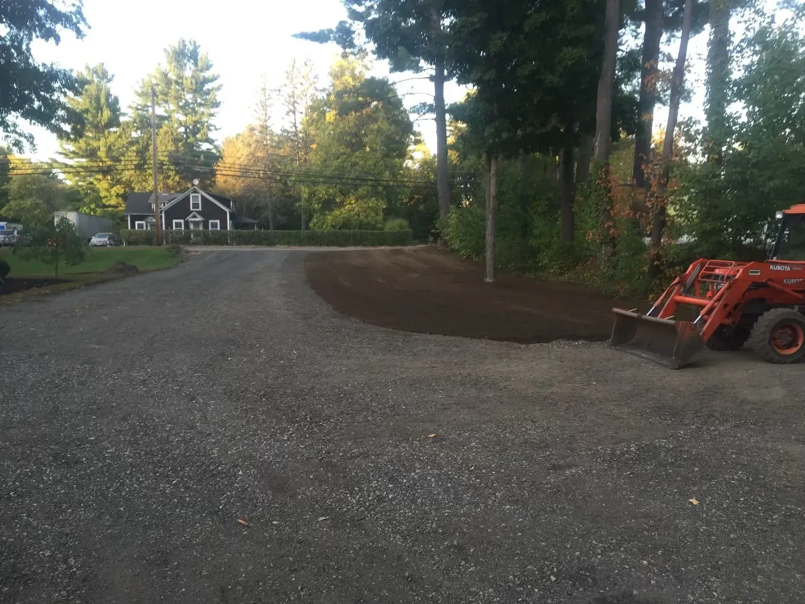Gravel driveway with a red tractor on the right and a house among trees in the background