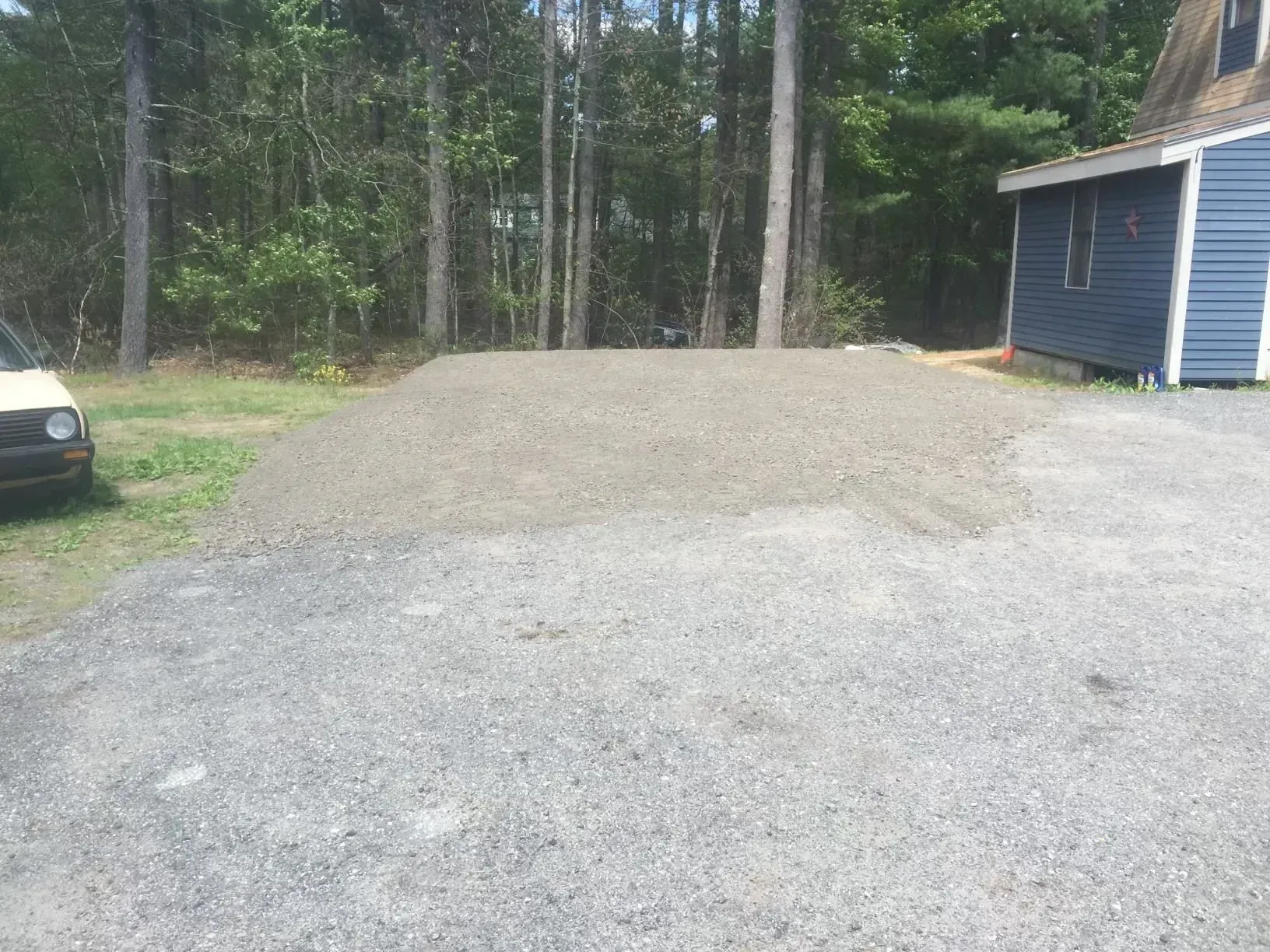 Gravel pile beside a blue house with a wooded area in the background