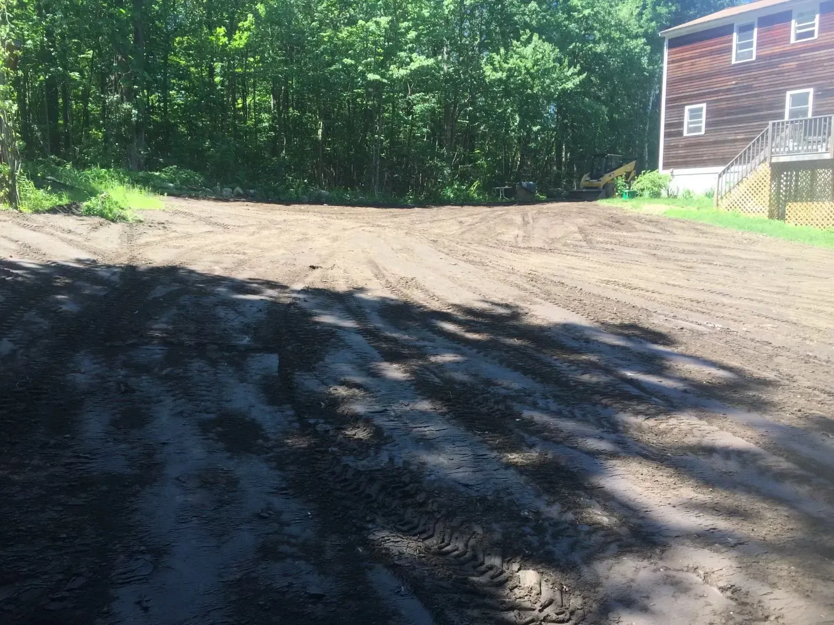 Gravel driveway beside a wooded area, with part of a house visible in the background.
