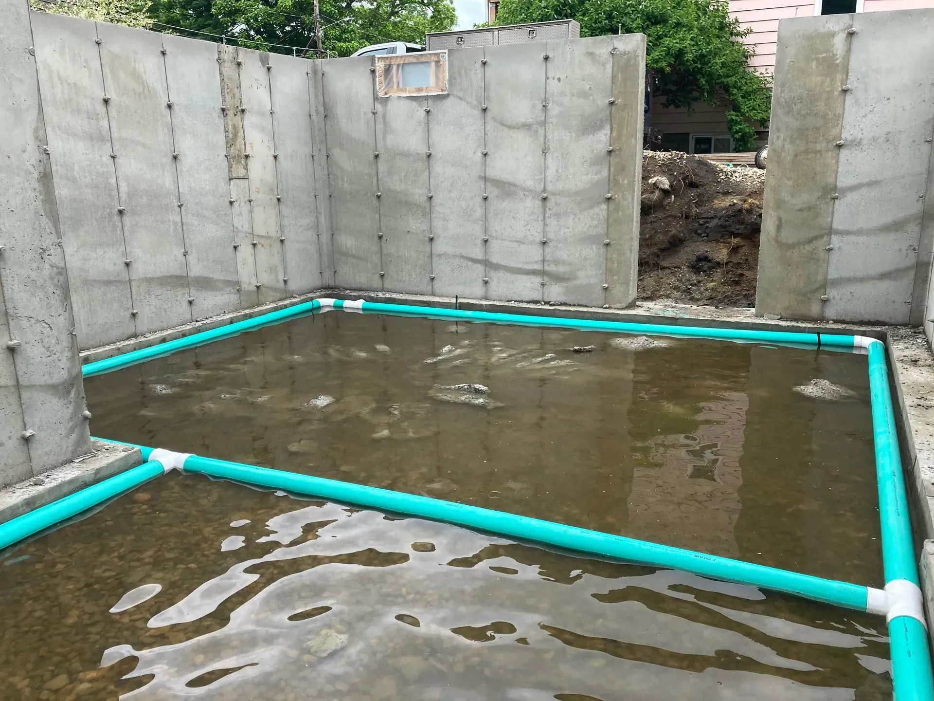 Flooded concrete foundation with turquoise PVC piping and muddy water inside an excavation site