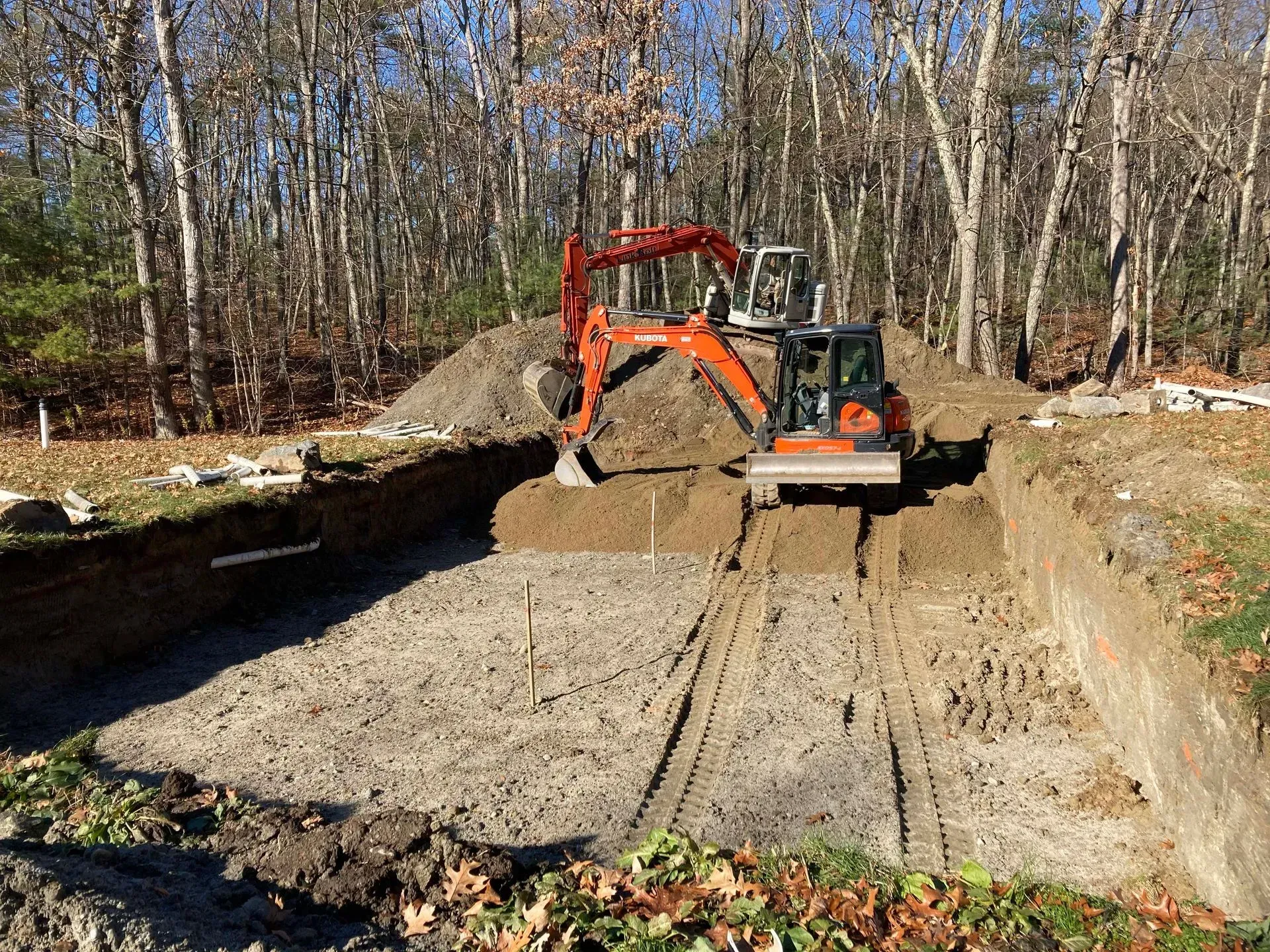 Orange excavator smoothing dirt in a wooded construction site