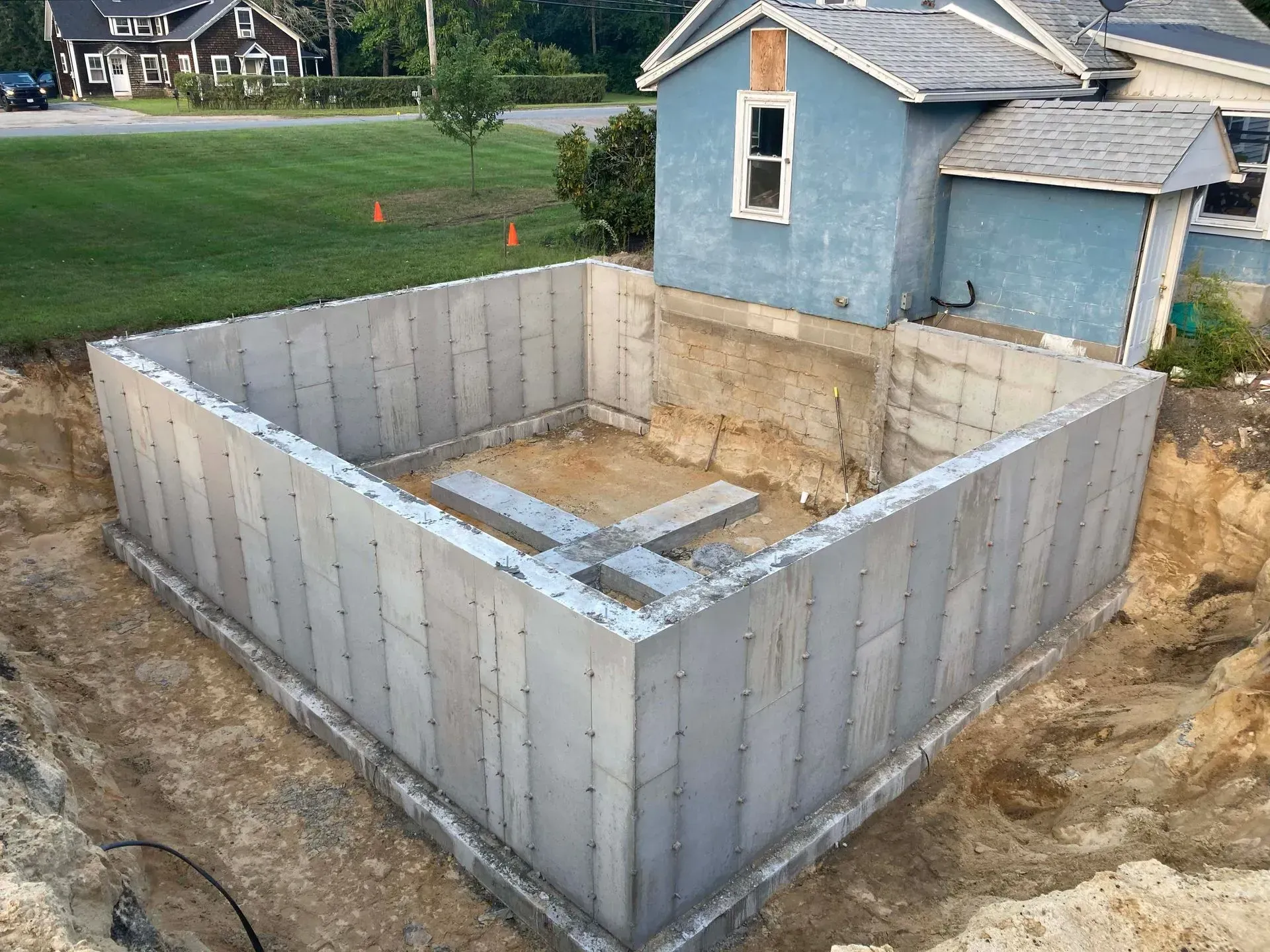 Concrete foundation walls for a house under construction beside a blue home in a suburban yard