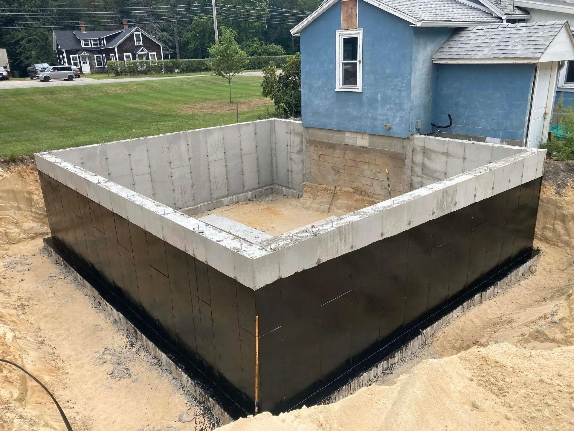 A large excavated dirt slope beside a concrete retaining wall with survey stakes and a stairway on the right.