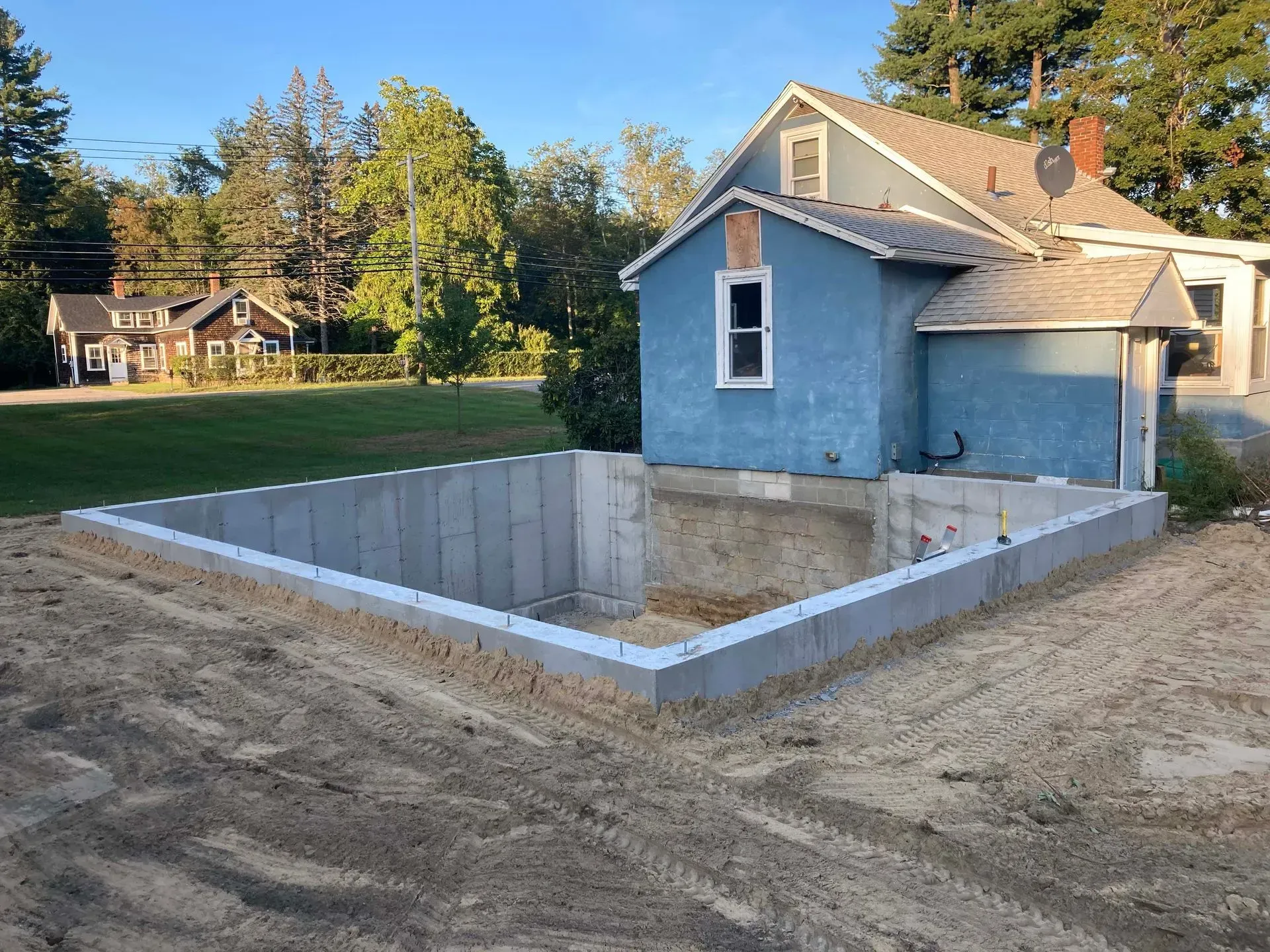 Backyard with a concrete basement foundation beside a blue house at dusk