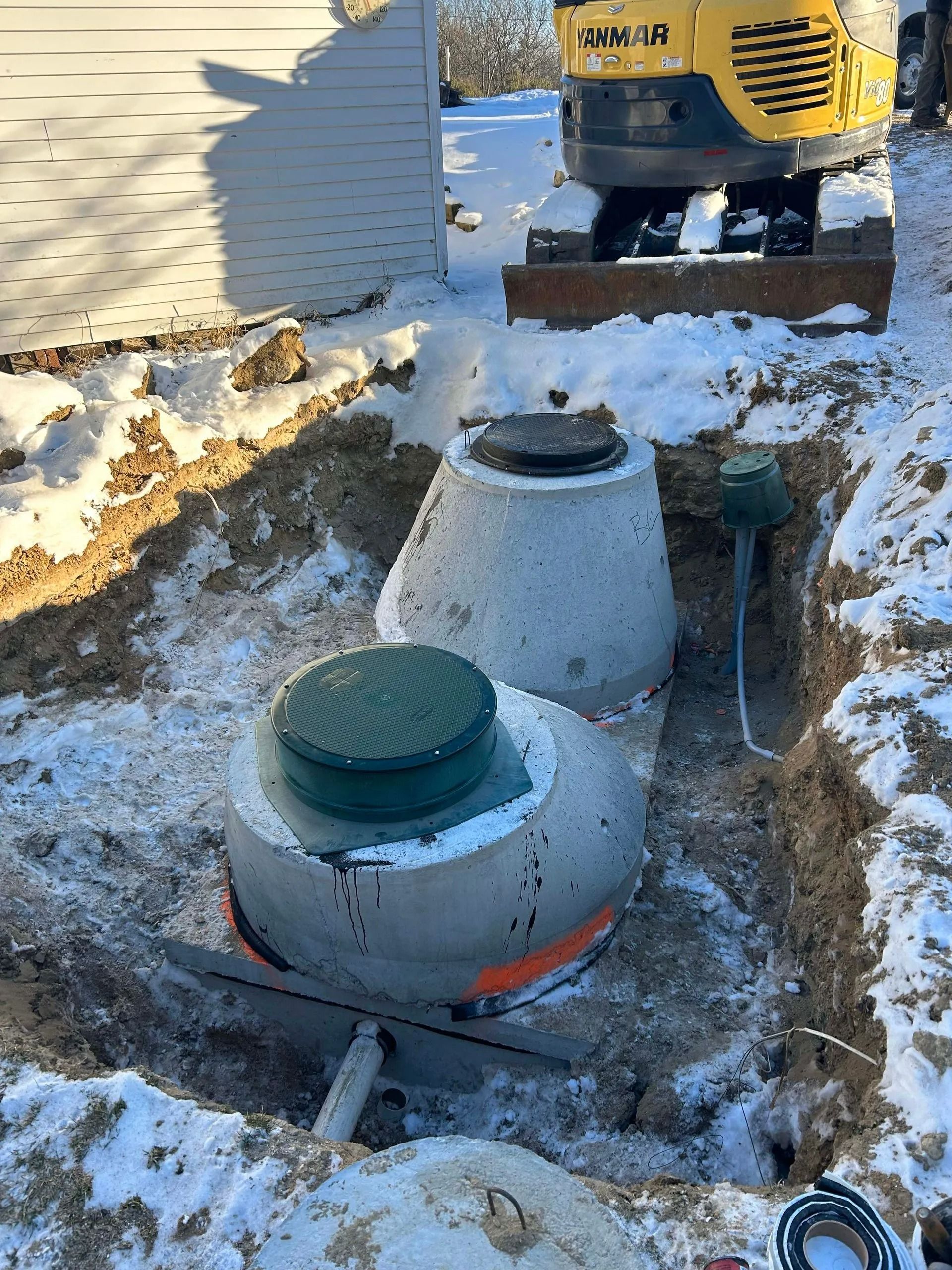Rectangular gray septic tank installed in a dirt excavation on a construction site.