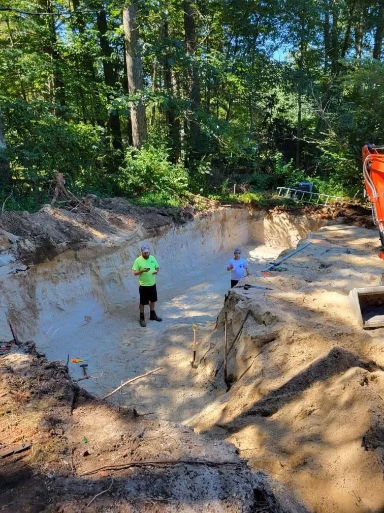 Large dirt excavation pit beside a building with stairs, surrounded by trees and bare ground.