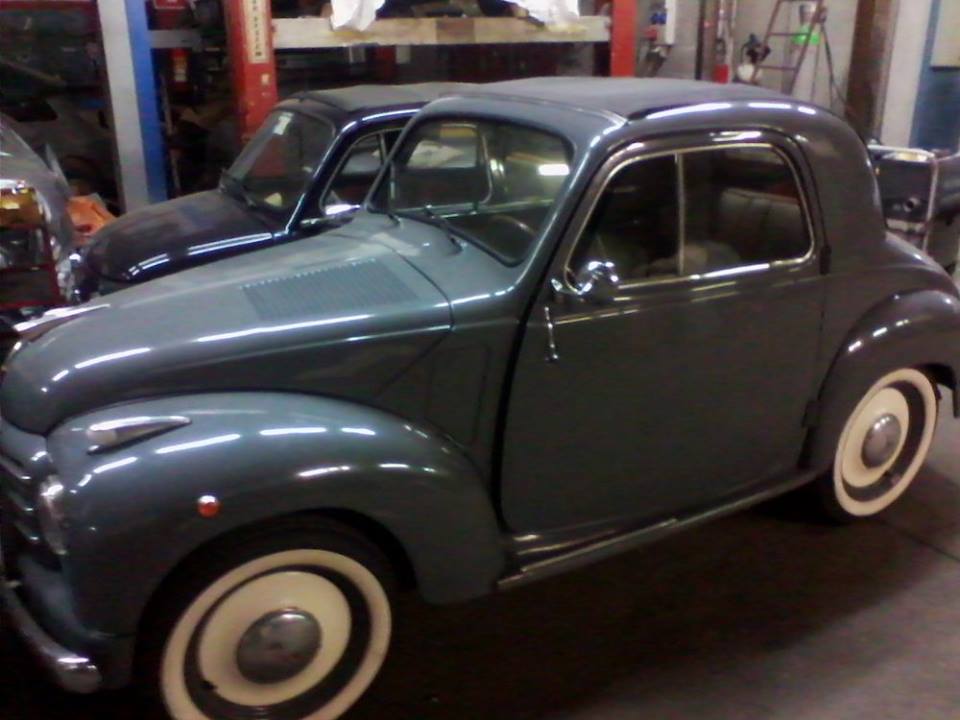 Fiat 500 coupé grigia d'epoca con pneumatici a fascia bianca, parcheggiata all'interno di un garage.