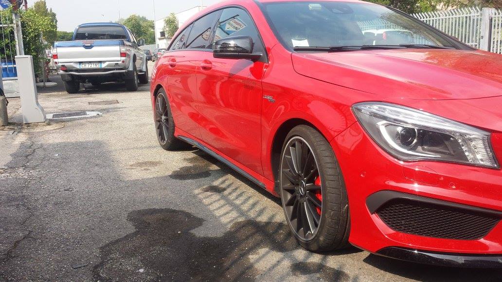 Una Mercedes-Benz CLA rossa parcheggiata su una superficie asfaltata bagnata. Sullo sfondo si vede un camion bianco.