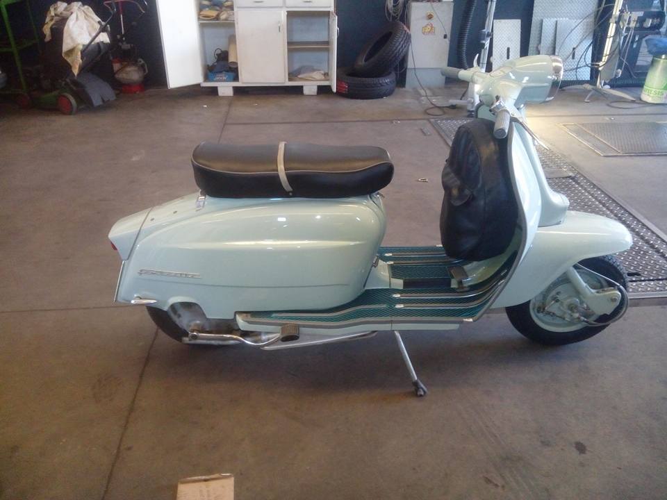 Scooter vintage azzurro con sedile nero, parcheggiato al chiuso.