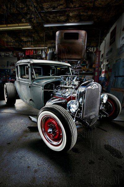 Hot rod grigia in un garage, con motore in mostra, cerchi rossi e pneumatici a fascia bianca.