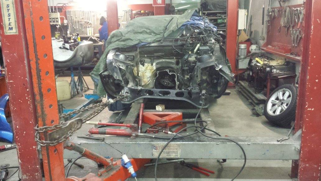 Carrozzeria su un ponte sollevatore in un'officina; sono visibili il motore coperto, gli attrezzi e un'altra auto.