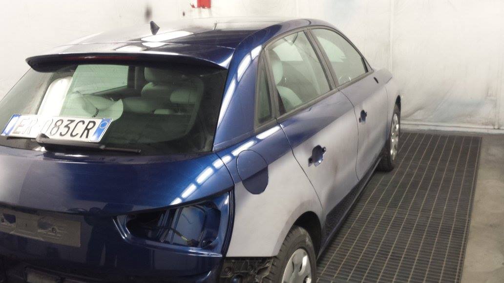 Auto blu in carrozzeria, con pannelli di colori diversi, la parte posteriore è in riparazione.