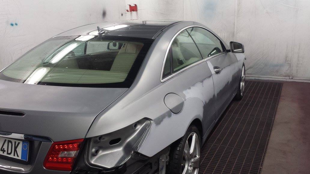 Auto grigia con danni in una cabina di verniciatura.