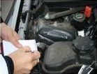 Persona che scrive su un blocco note nel vano motore di un'auto, valutando i componenti.