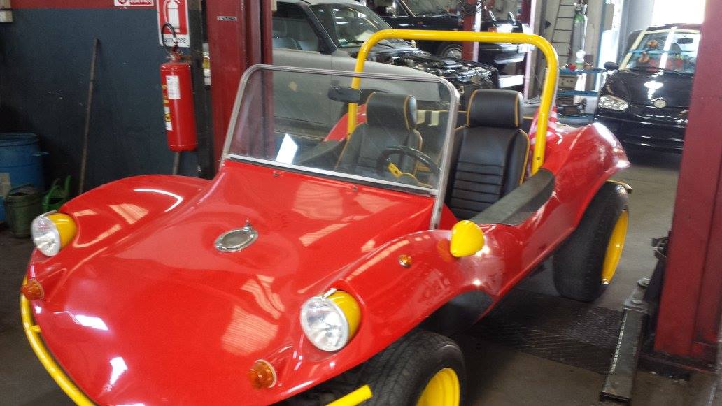 Buggy da spiaggia rosso con roll bar e ruote gialle, in un garage.