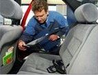 Un uomo con una camicia da lavoro blu, all'interno di un'auto, controlla una cintura di sicurezza.