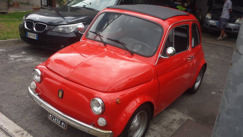 Fiat 500 rossa con tetto nero, parcheggiata su una superficie asfaltata. Sullo sfondo c'è un'auto nera.