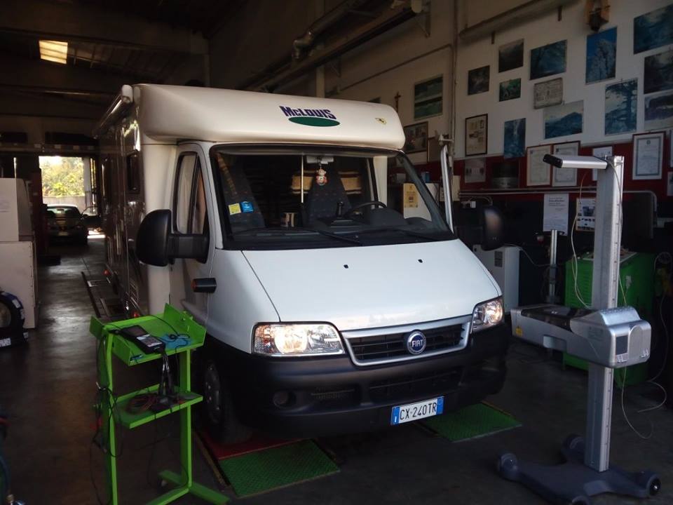 Camper bianco in un garage in fase di ispezione; sono visibili il carrello portautensili verde e l'attrezzatura per l'ispezione.