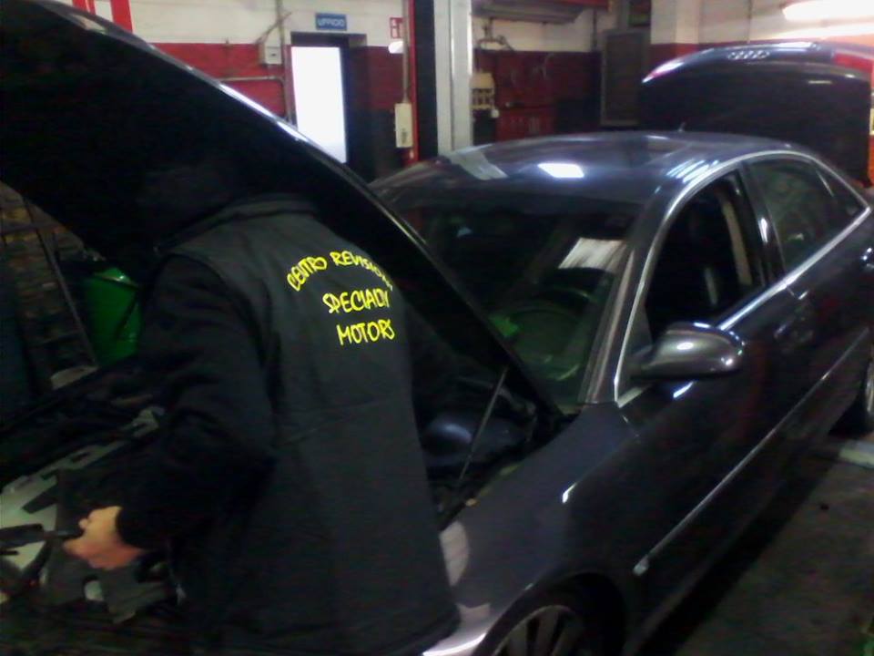 Meccanico in uniforme nera al lavoro su un'auto con il cofano aperto in un garage.