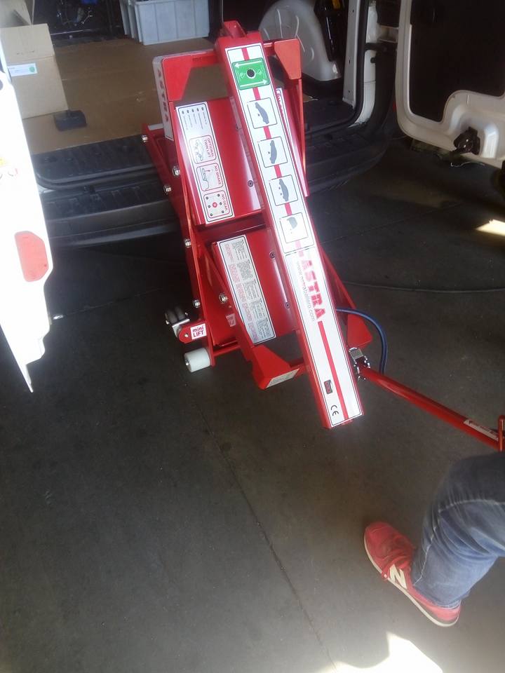 Ponte sollevatore per veicoli Astra rosso con il piede di una persona visibile, in un'officina di riparazione.