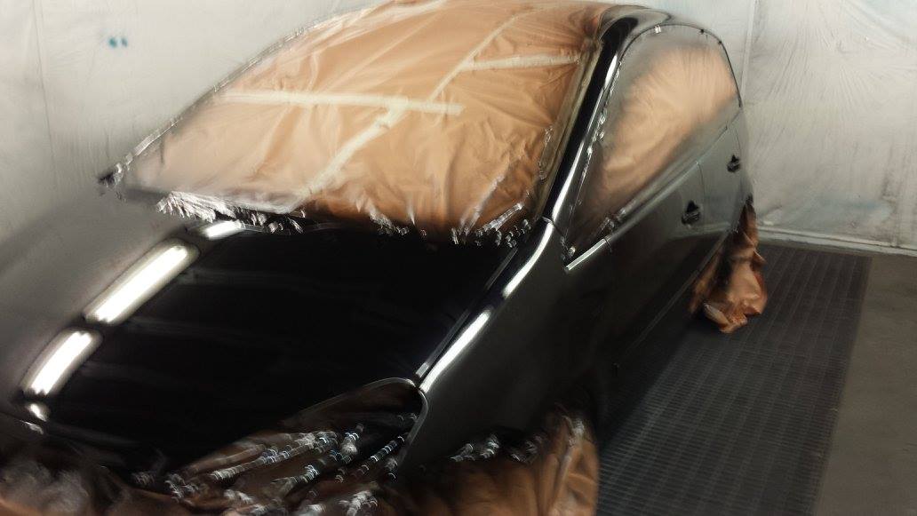 Pannello nero di un'auto in fase di verniciatura in una cabina di verniciatura; parabrezza mascherato.