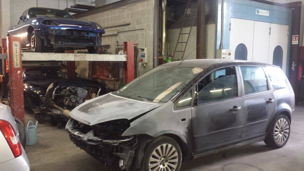 Carrozzeria: auto grigia in riparazione, altri veicoli su un ponte sollevatore e sullo sfondo.
