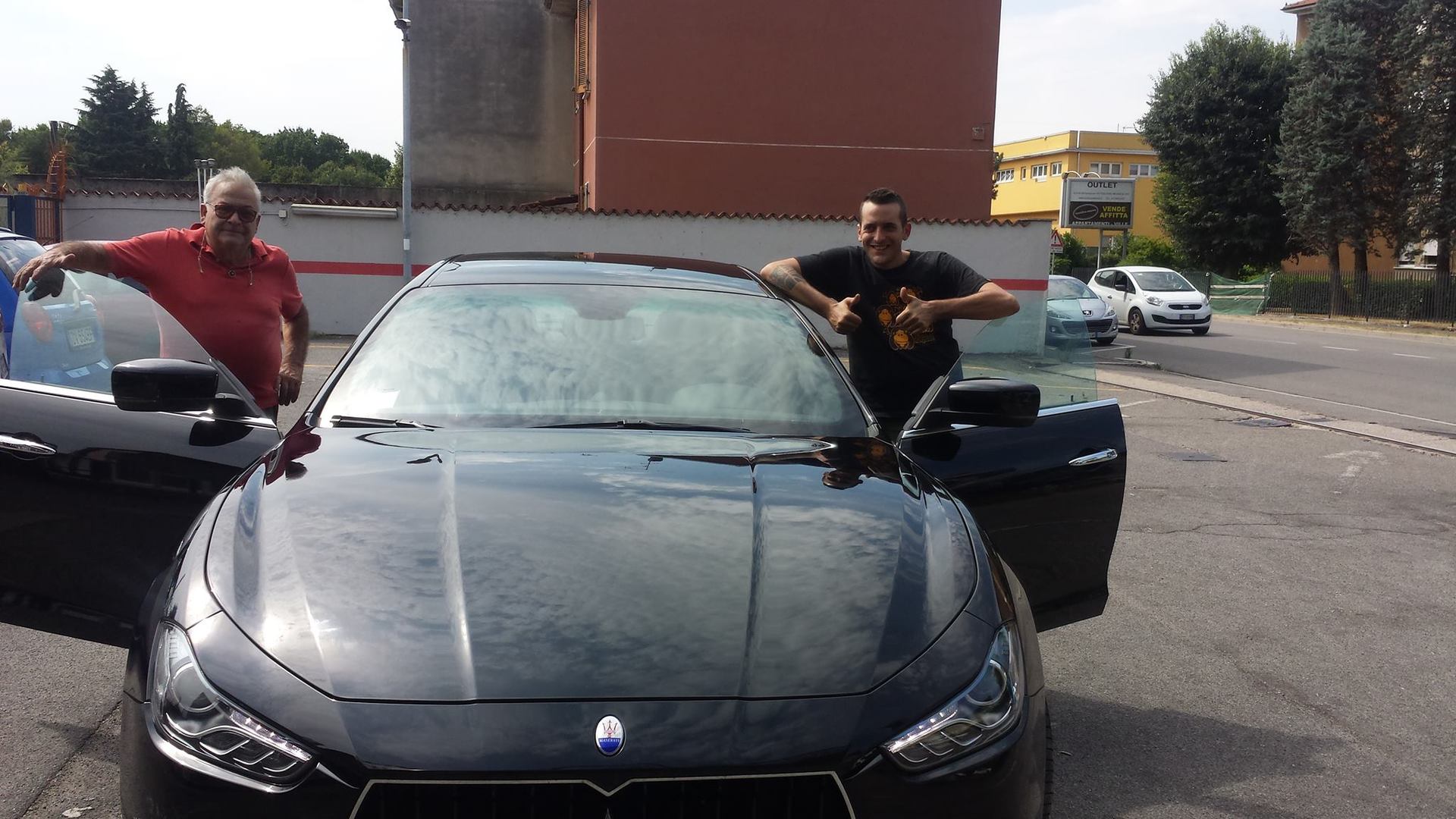 Due uomini sono in piedi accanto a una Maserati nera con le portiere aperte in un parcheggio.